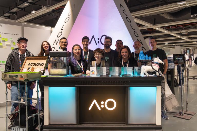 Ein Team von elf Personen steht hinter einem Ausstellungstisch mit A:O-Logo, in einer Messehalle.